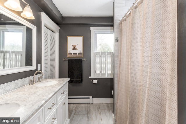 bathroom with a baseboard heating unit, a sink, baseboards, a closet, and double vanity