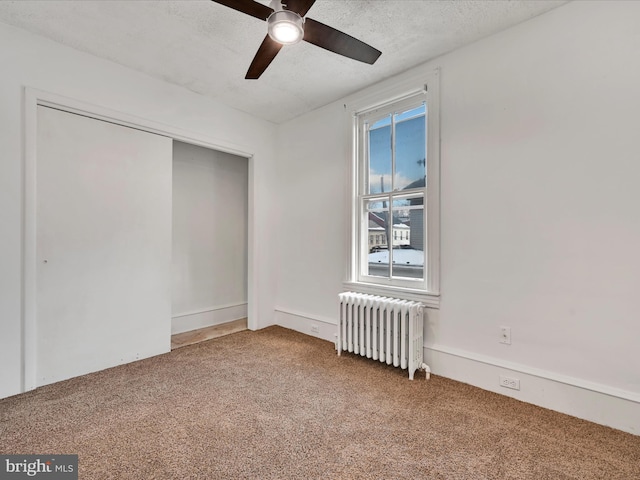 carpeted spare room with ceiling fan, radiator heating unit, and a textured ceiling