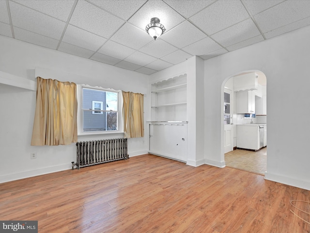 unfurnished living room featuring radiator, a drop ceiling, and light hardwood / wood-style flooring