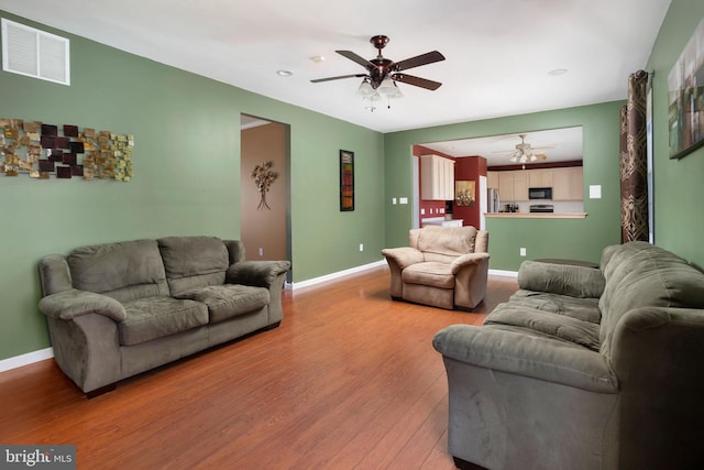 living room featuring a ceiling fan, baseboards, visible vents, and light wood finished floors