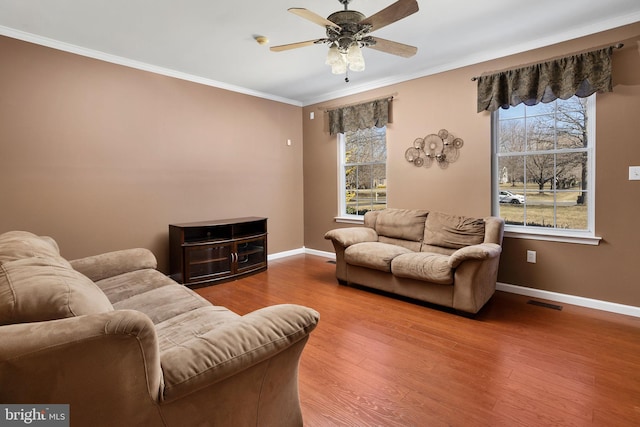 living area with wood finished floors, a ceiling fan, visible vents, baseboards, and ornamental molding