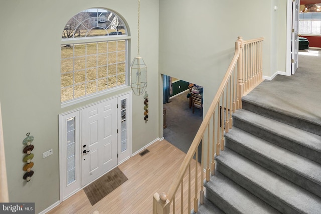 entryway with a towering ceiling, stairs, baseboards, and wood finished floors