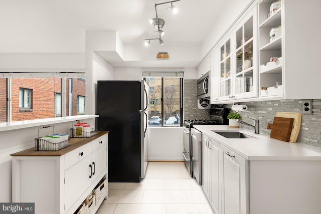 kitchen featuring appliances with stainless steel finishes, sink, white cabinets, tasteful backsplash, and light tile patterned floors