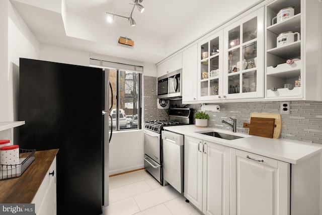 kitchen with appliances with stainless steel finishes, sink, white cabinets, backsplash, and light tile patterned flooring