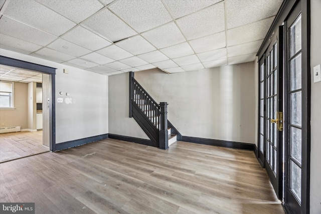 unfurnished room with baseboard heating, a paneled ceiling, and wood-type flooring