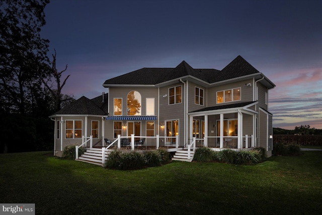 back house at dusk with a lawn and covered porch