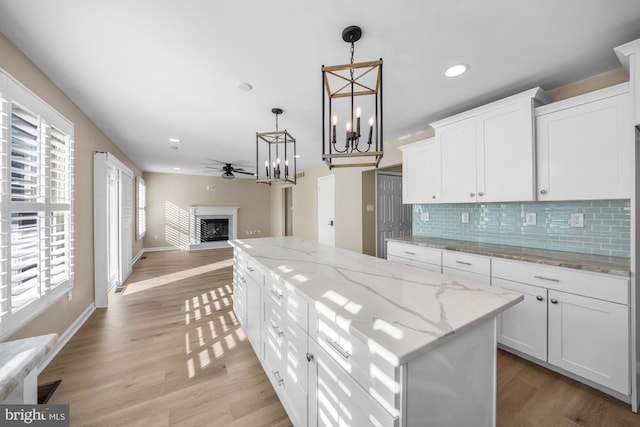 kitchen with decorative light fixtures, white cabinetry, a center island, light stone counters, and ceiling fan with notable chandelier