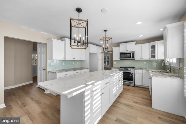 kitchen featuring sink, white cabinets, decorative light fixtures, a kitchen island, and appliances with stainless steel finishes