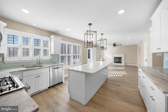 kitchen featuring hanging light fixtures, a kitchen island, white cabinets, stainless steel dishwasher, and sink