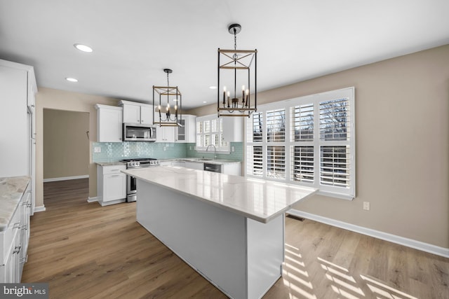 kitchen featuring appliances with stainless steel finishes, hanging light fixtures, a center island, sink, and white cabinetry