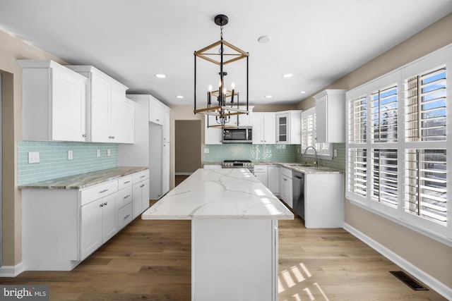 kitchen featuring hanging light fixtures, a center island, stainless steel appliances, white cabinetry, and sink