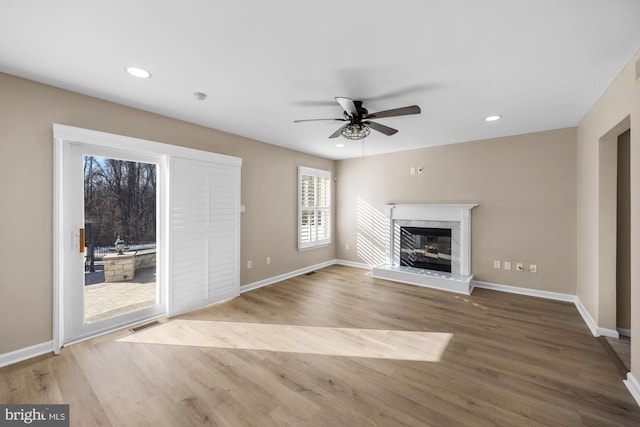 unfurnished living room featuring a premium fireplace, ceiling fan, and light wood-type flooring