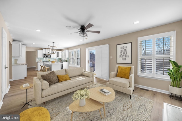 living room featuring ceiling fan with notable chandelier and light hardwood / wood-style flooring