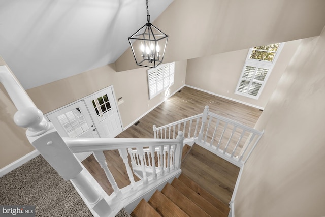 stairs featuring hardwood / wood-style floors, high vaulted ceiling, and a chandelier