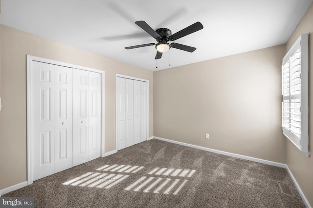 unfurnished bedroom with ceiling fan, two closets, multiple windows, and carpet flooring