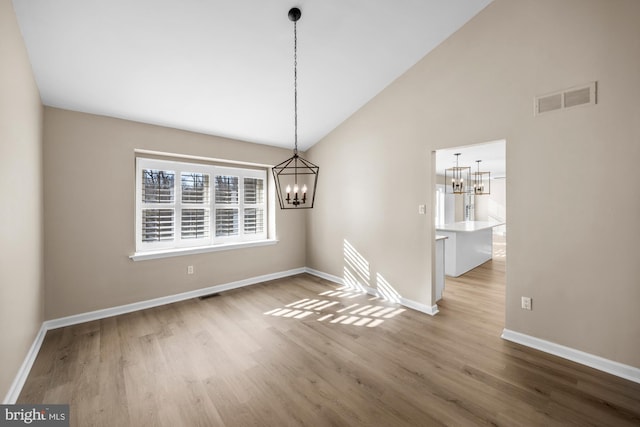 unfurnished dining area with wood-type flooring, high vaulted ceiling, and a notable chandelier