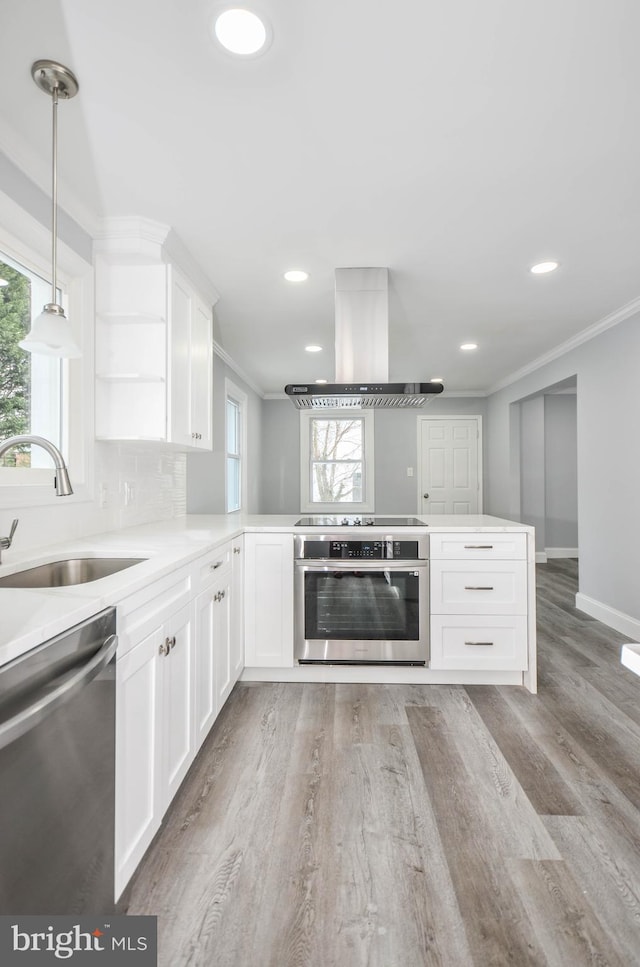 kitchen featuring kitchen peninsula, island range hood, white cabinets, and appliances with stainless steel finishes