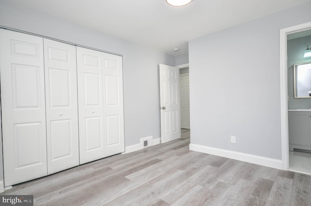 unfurnished bedroom featuring ensuite bathroom, a closet, and light hardwood / wood-style floors