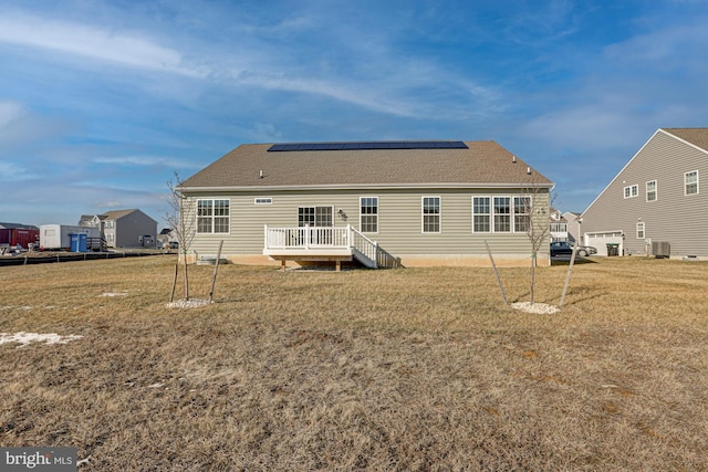 rear view of property featuring a lawn, cooling unit, solar panels, and a wooden deck