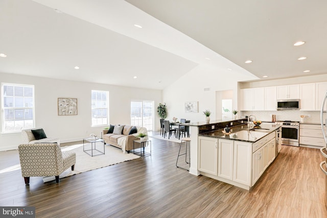 kitchen with vaulted ceiling, stainless steel appliances, a kitchen island with sink, dark stone counters, and a kitchen breakfast bar