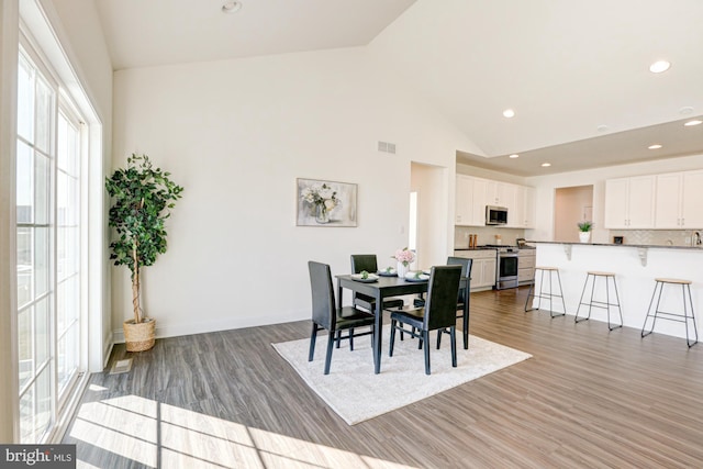 dining room with high vaulted ceiling and wood-type flooring