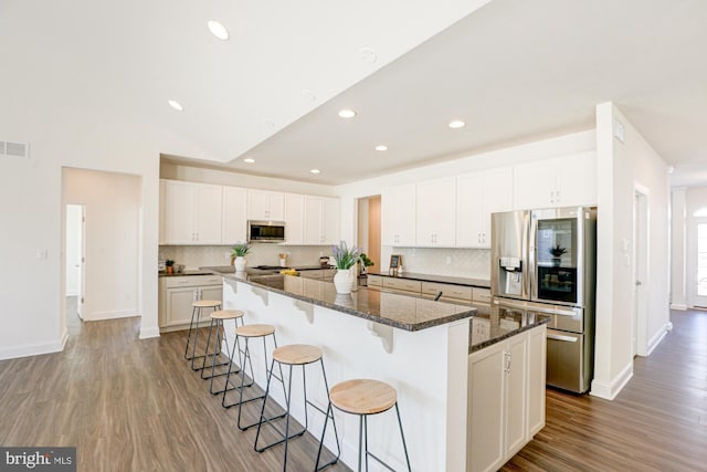 kitchen with a large island, hardwood / wood-style floors, stainless steel appliances, dark stone counters, and white cabinets