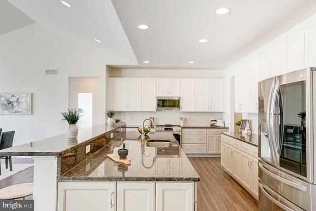 kitchen featuring appliances with stainless steel finishes, white cabinetry, dark stone countertops, and sink