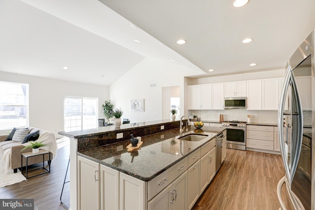 kitchen with vaulted ceiling, stainless steel appliances, a kitchen island with sink, dark stone countertops, and sink