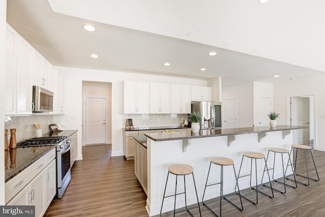 kitchen featuring stainless steel appliances, an island with sink, a breakfast bar area, white cabinets, and dark stone countertops