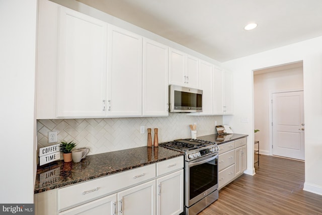 kitchen featuring dark stone counters, stainless steel appliances, white cabinetry, and decorative backsplash