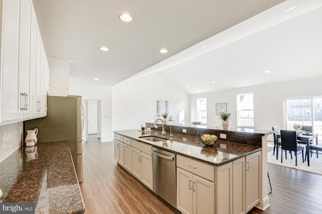 kitchen featuring dishwasher, a center island with sink, hardwood / wood-style floors, dark stone counters, and sink