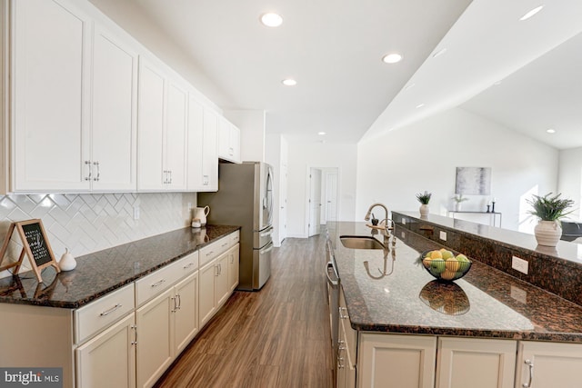 kitchen featuring hardwood / wood-style flooring, vaulted ceiling, backsplash, dark stone counters, and sink