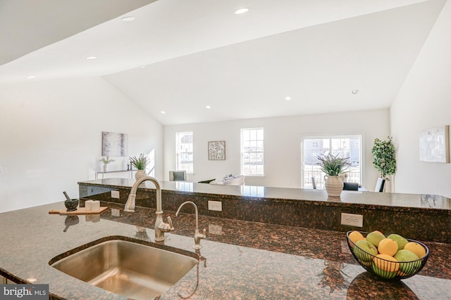 kitchen with sink, lofted ceiling, and dark stone counters