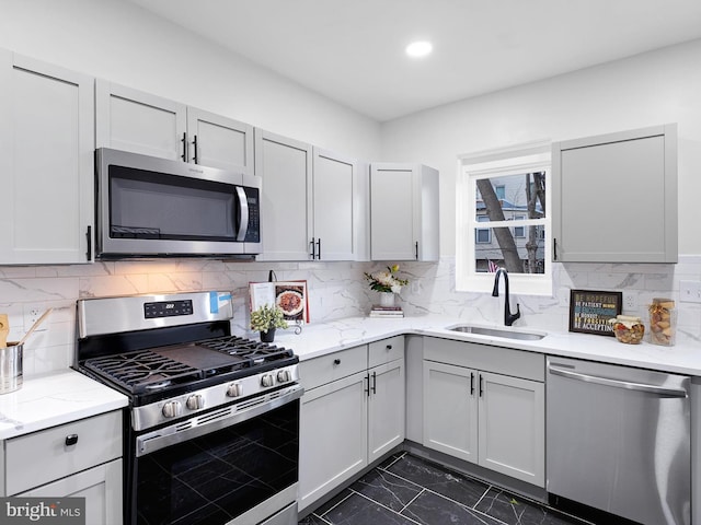 kitchen with light stone countertops, appliances with stainless steel finishes, backsplash, sink, and gray cabinets