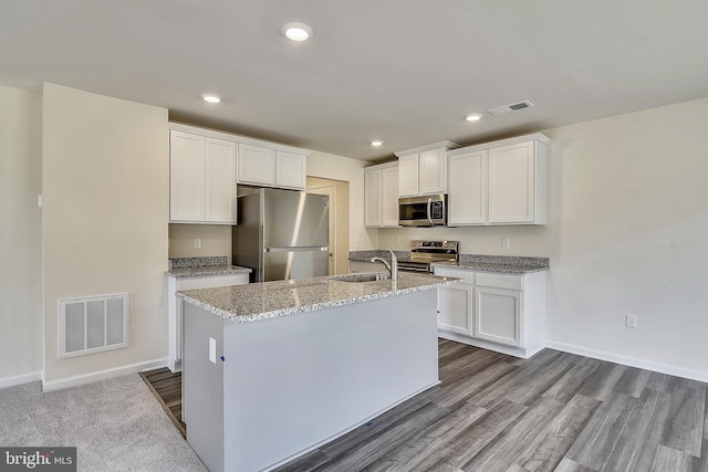 kitchen featuring light stone countertops, stainless steel appliances, a kitchen island with sink, sink, and white cabinets