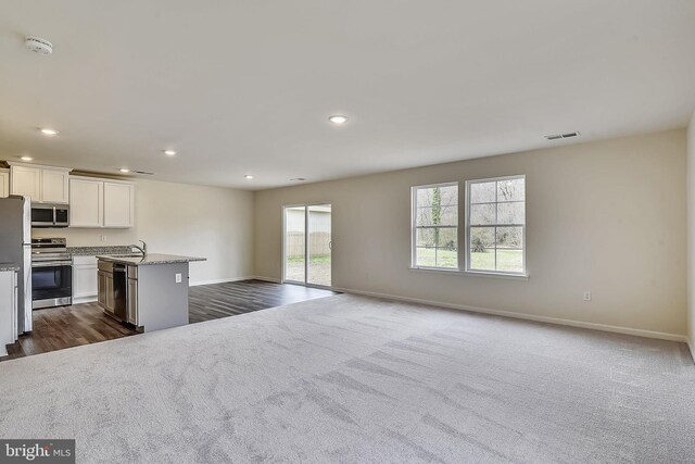 kitchen with a kitchen island with sink, sink, light stone countertops, white cabinetry, and stainless steel appliances