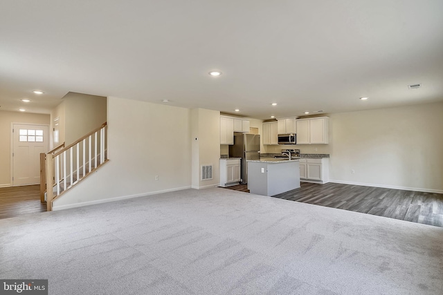 kitchen featuring sink, stainless steel appliances, dark colored carpet, a kitchen island with sink, and white cabinets