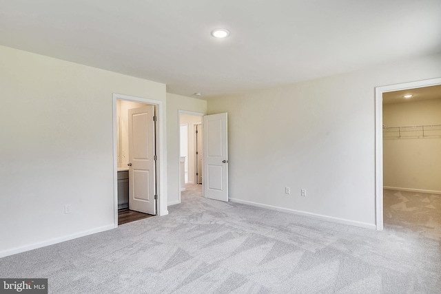 unfurnished bedroom featuring light carpet, ensuite bath, a spacious closet, and a closet