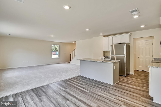 kitchen featuring light stone countertops, stainless steel fridge, a center island with sink, light hardwood / wood-style floors, and white cabinetry