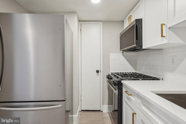 kitchen with light stone countertops, white cabinets, appliances with stainless steel finishes, tasteful backsplash, and light hardwood / wood-style floors