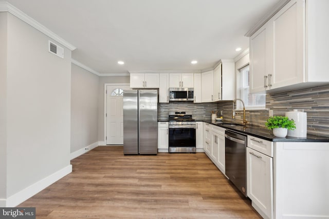 kitchen with light hardwood / wood-style floors, appliances with stainless steel finishes, tasteful backsplash, sink, and white cabinets