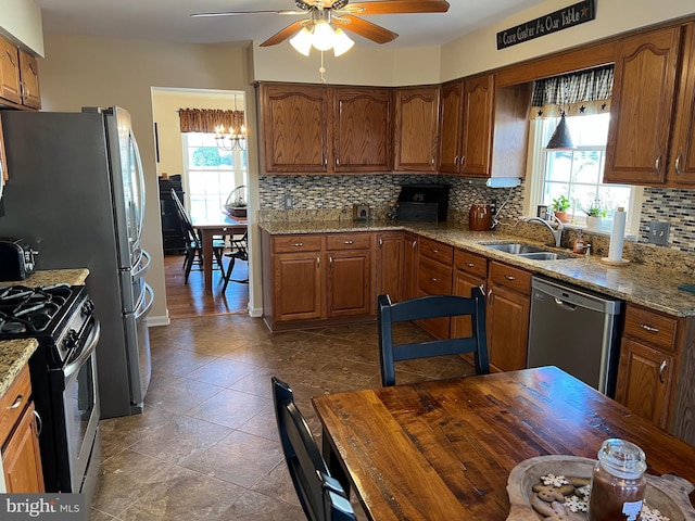 kitchen featuring appliances with stainless steel finishes, ceiling fan with notable chandelier, light stone counters, sink, and tasteful backsplash