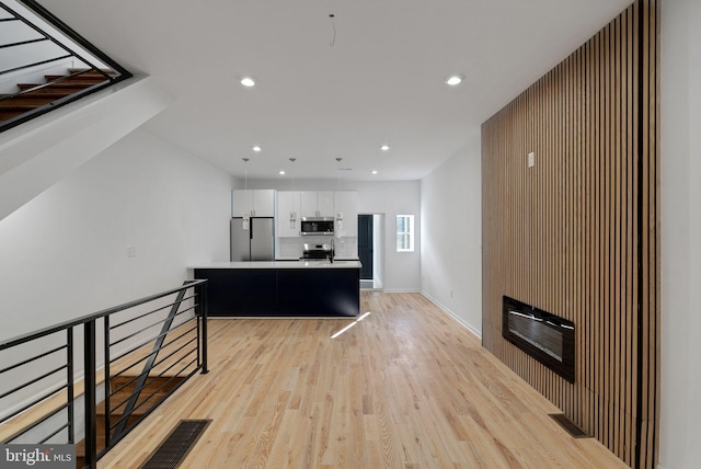 kitchen with stainless steel appliances, decorative light fixtures, white cabinetry, a center island, and light hardwood / wood-style floors