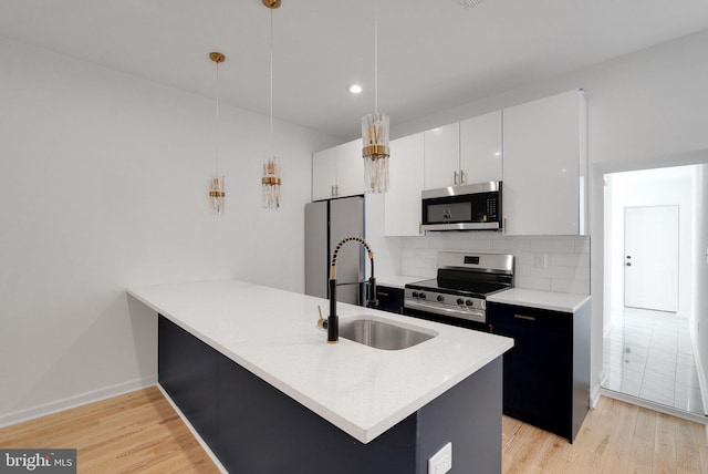 kitchen featuring pendant lighting, stainless steel appliances, tasteful backsplash, light wood-type flooring, and white cabinetry