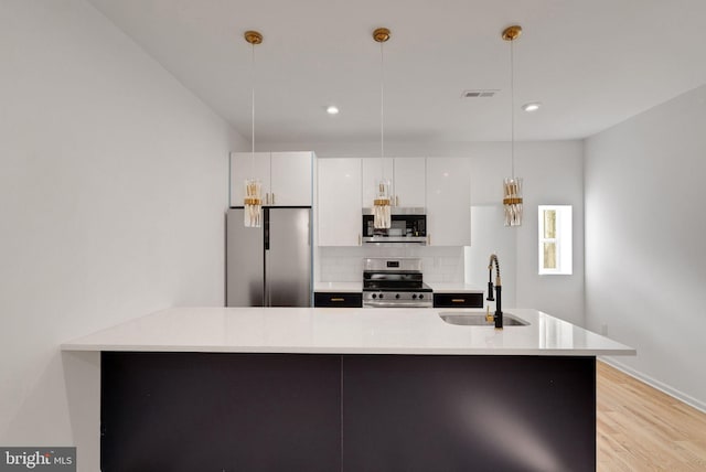 kitchen with stainless steel appliances, white cabinetry, sink, and hanging light fixtures