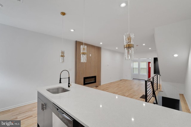 kitchen featuring a large fireplace, light stone countertops, dishwasher, pendant lighting, and sink