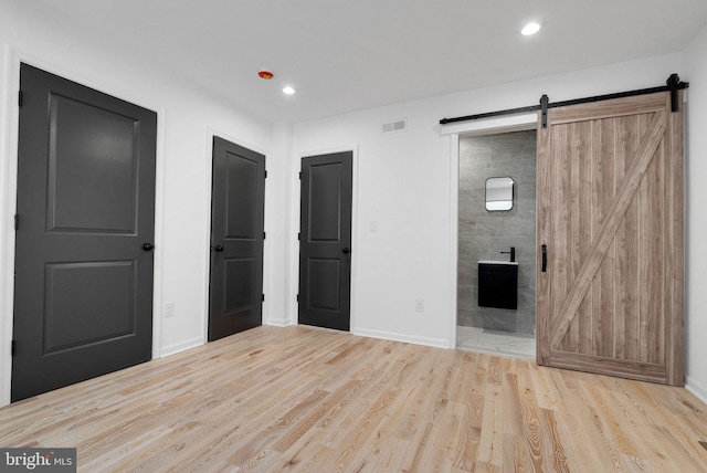 unfurnished bedroom with ensuite bathroom, a barn door, and light hardwood / wood-style floors