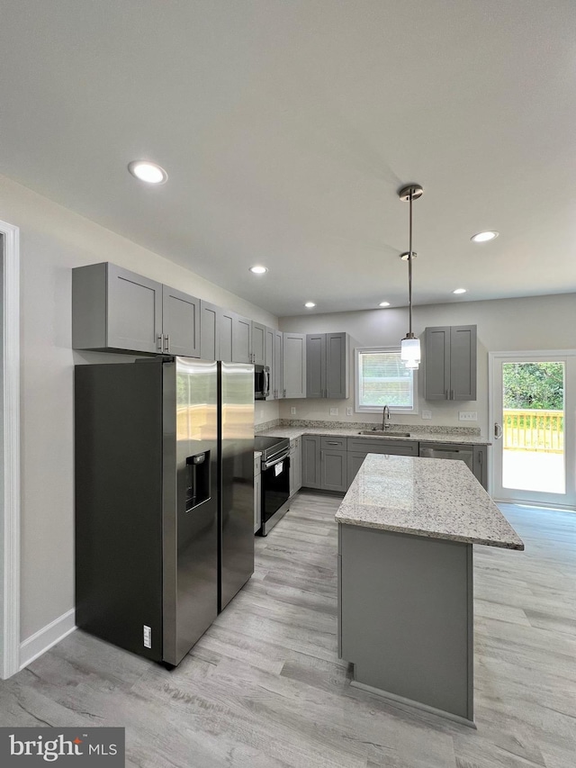 kitchen featuring sink, a center island, light stone counters, pendant lighting, and appliances with stainless steel finishes