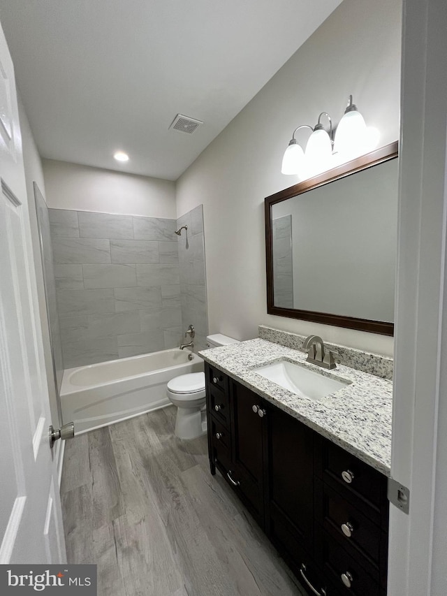 full bathroom featuring hardwood / wood-style floors, vanity, tiled shower / bath combo, and toilet