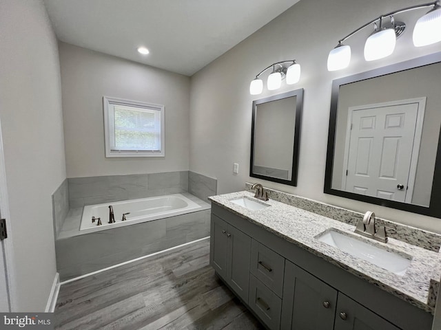 bathroom with hardwood / wood-style floors, vanity, and tiled bath